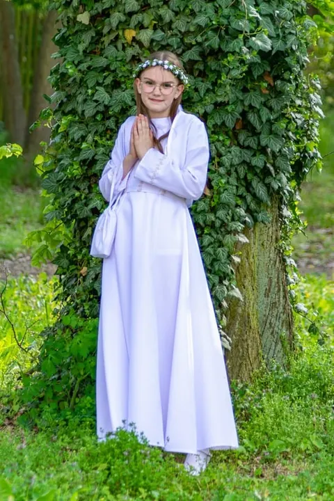 Dziewczynka w stroju komunijnym na tle bluszczu